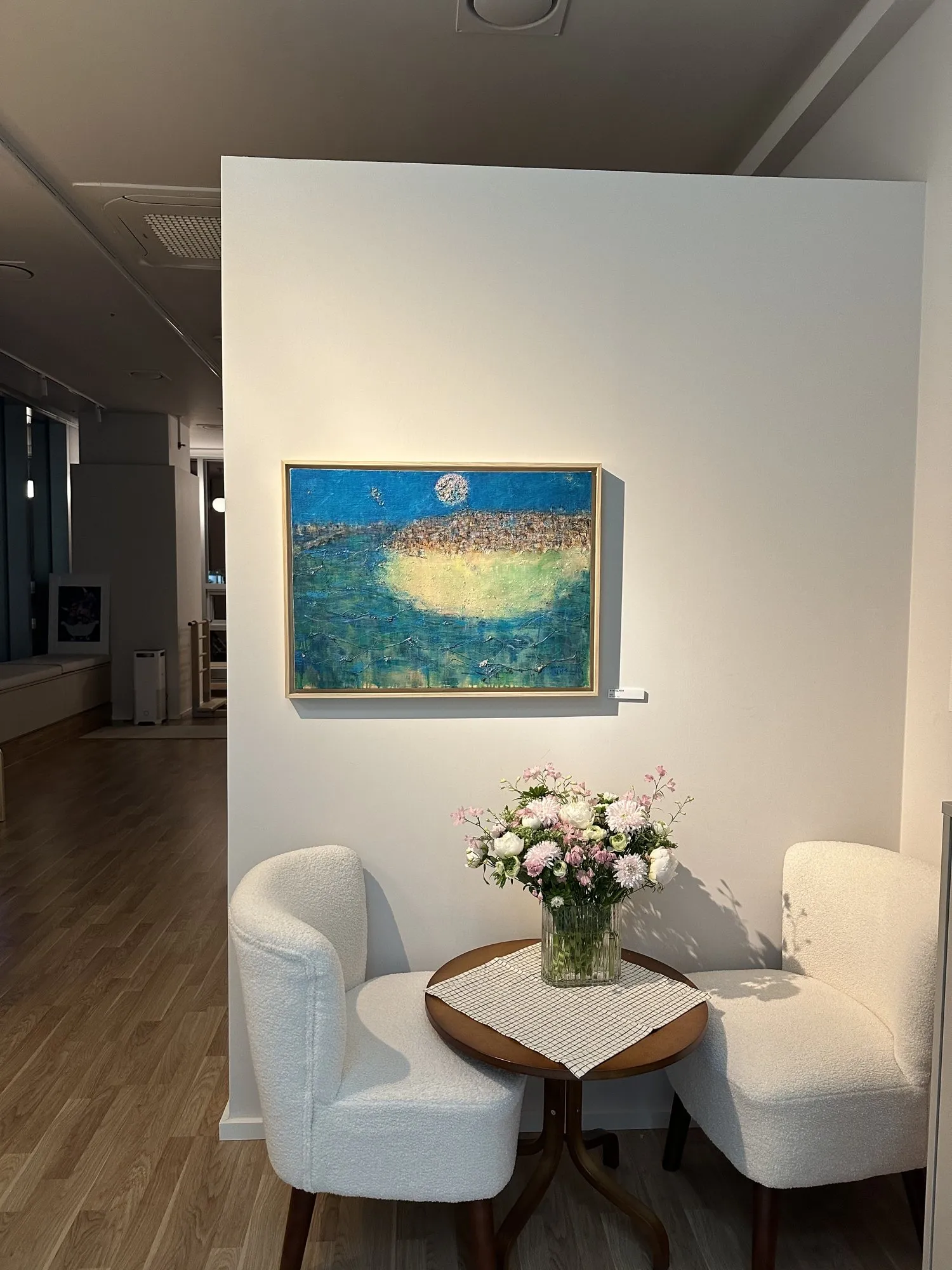 바다 그림 아래 흰 의자 두 개와 꽃이 놓인 라운지